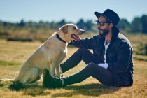 Портрет молодого татуйованого чоловіка, який грає зі своїм собакою в сільській місцевості — стокове фото