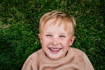 Счастливый мальчик, лежа в траве улыбаясь — стоковое фото