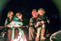 Grandparents and grandchildren sitting around fire pit laughing — Stock Photo