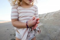 Детальний знімок маленької дівчинки, що тримає мушлі на пляжі з сукнею на — стокове фото