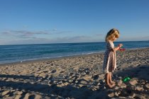 Little girl looking at her hands with back to the ocean on the beach — Stock Photo