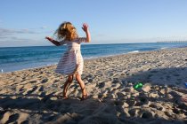 Kleines Mädchen tanzt am Strand bei blauem Himmel — Stockfoto