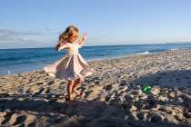 Petite fille dansant sur la plage avec un ciel bleu — Photo de stock