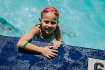 Маленька дівчинка тримається на боці басейну, дивлячись вгору і посміхаючись — стокове фото