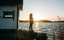 Людина стояла на скелі біля дерев'яної хатини в Швеції на заході сонця. — стокове фото