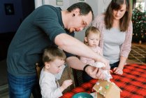 Сім'я з маленькими дітьми прикрашає імбирний будинок у грудні — стокове фото