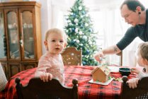 Family with little children decorating a gingerbread house in December — Stock Photo