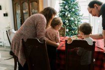 Семья с маленькими детьми, украшающими пряничный домик в декабре — стоковое фото