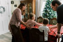 Família com crianças pequenas decorando uma casa de gengibre em dezembro — Fotografia de Stock