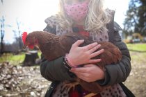 Gros plan d'une fille portant un masque tenant du poulet dans une ferme — Photo de stock