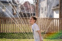 Хлопчик грає у воді спринклер на задньому дворі — стокове фото