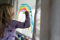 Блондинка рисует радугу на окне интерьера в доме — стоковое фото