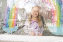 Девушка смотрит в сторону под радугу, нарисованную на окне — стоковое фото