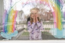 Fora em vista de menina bonito sob arco-íris pintado na janela — Fotografia de Stock