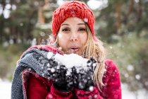 Portrait of happy young woman playing with snow in winter, blowing snowflakes to camera, copy space — Stock Photo