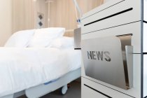 Cama blanca con caja de noticias en la habitación del hospital - foto de stock