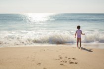 A little girl stands at the edge of the shore with oncoming wave — Stock Photo