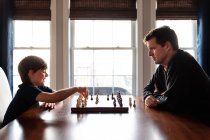 Padre e figlio seduti a un tavolo in casa a giocare a scacchi. — Foto stock