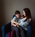 Happy woman hugging her smiling son as he sits in her lap on a chair. — Stock Photo