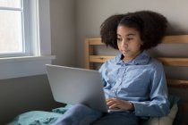 Elfjähriges zweirassiges Mädchen arbeitet auf Laptop im Bett — Stockfoto
