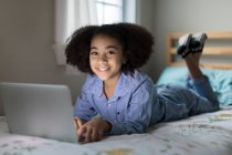 Одиннадцатилетняя двухрасовая девочка работает на ноутбуке в постели — стоковое фото