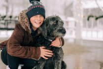 Хлопчик обіймає собаку в сніжний зимовий день — стокове фото