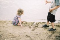 Two children playing in the sand by the shore of a lake — Stock Photo