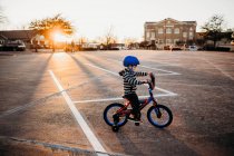 Молодий хлопчик їде на велосипеді з тренувальними колесами на парковці на заході сонця — стокове фото
