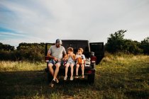 Papá y dos niños haciendo un picnic en el portón trasero del camión - foto de stock