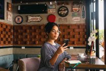 Mujer joven con teléfono móvil y taza de café en la cafetería - foto de stock