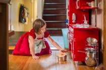 Маленькая девочка в фартуке и платье для вечеринки играет с игрушечной кухней — стоковое фото