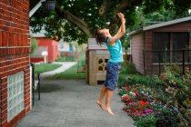 Ein kleiner Junge springt mit ausgestreckten Armen im schönen Garten in die Luft — Stockfoto