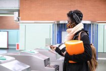 Африканская студентка университета в защитной маске проходит через турникеты с транспортной картой на станции метро. Новая норма в общественном транспорте. — стоковое фото