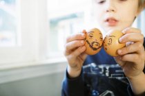Маленький мальчик притворяется, что играет с пасхальными яйцами с глупыми мультяшными лицами — стоковое фото