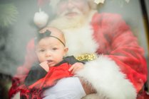 Bambino siede sulle ginocchia di Babbo Natale in finestra — Foto stock
