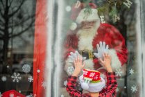 Menino jovem se conecta com Papai Noel na janela — Fotografia de Stock