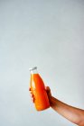 Mão feminina segurando garrafa de laranja com frutas frescas no fundo de cor — Fotografia de Stock