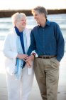 Портрет пожилой супружеской пары, держащейся за руки и смеющейся на пляже — стоковое фото