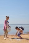 Hija y madre recogieron botellas de plástico junto al lago juntos - foto de stock