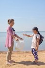 Hija y madre recogieron botellas de plástico junto al lago juntos - foto de stock