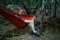 Junger Mann ruht mit seinem Smartphone auf einer Hängematte im Wald — Stockfoto