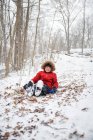 Щасливий хлопчик спустився на пагорб в лісі в сніжний зимовий день . — стокове фото