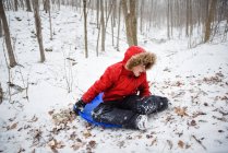 Rapaz feliz a descer uma colina na floresta num dia de inverno nevado. — Fotografia de Stock