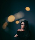 Pensive jolie femme dans la chambre noire avec bokeh lumière entourant son — Photo de stock