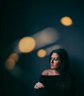 Pensiva mulher bonita no quarto escuro com luz bokeh em torno dela — Fotografia de Stock