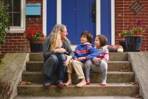 Eine lächelnde Mutter sitzt mit ihren beiden Kindern vor der Haustür — Stockfoto