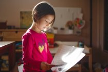 Маленька дівчинка в красивому світлі читає з листів паперу — стокове фото