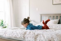 Pequena menina criança independente na cama lendo um livro de história sozinho — Fotografia de Stock
