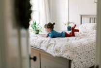 Pequeña niña independiente en la cama leyendo un libro de cuentos sola - foto de stock