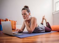 Mulher praticando ioga com computador portátil em sua casa — Fotografia de Stock